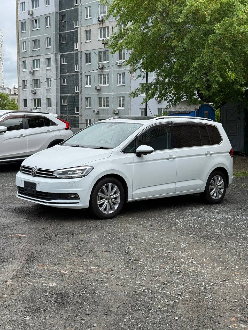 Белый Volkswagen Touran из Японии на стоянке во Владивостоке, вид спереди 3/4