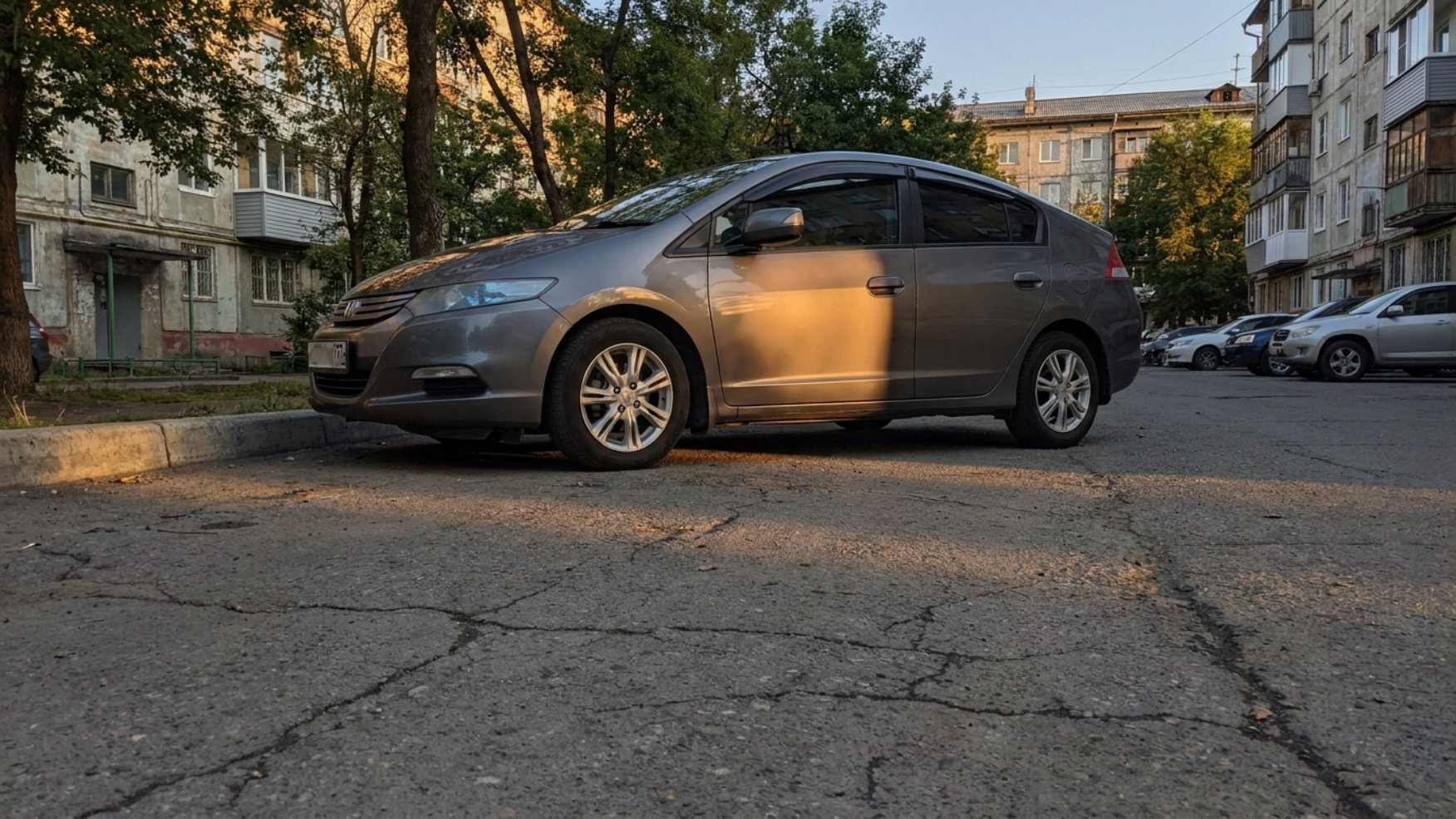 Honda Insight припаркован во дворе Владивостока у высокого бордюра, вечерний свет