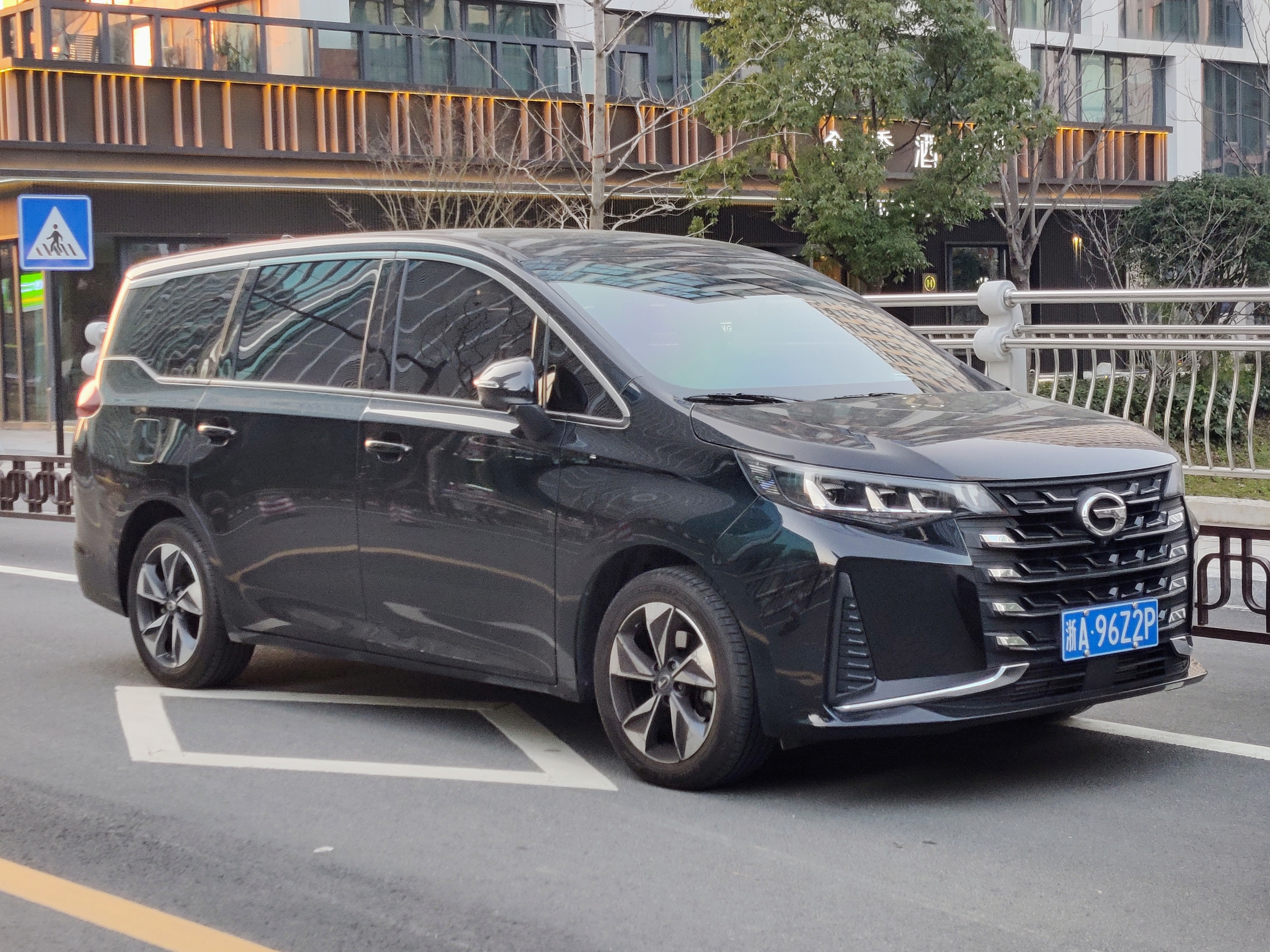 Тёмно-зелёный GAC Trumpchi M6 у обочины в китайском городе, реальное фото, вид сбоку 3/4